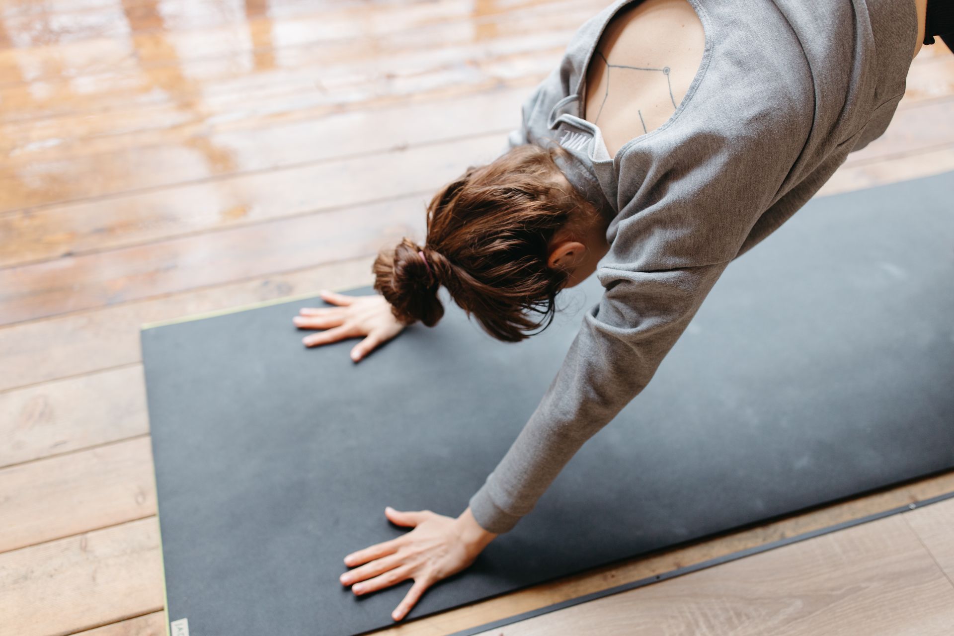 A woman stretching forward on a yoga mat on a wooden floor
