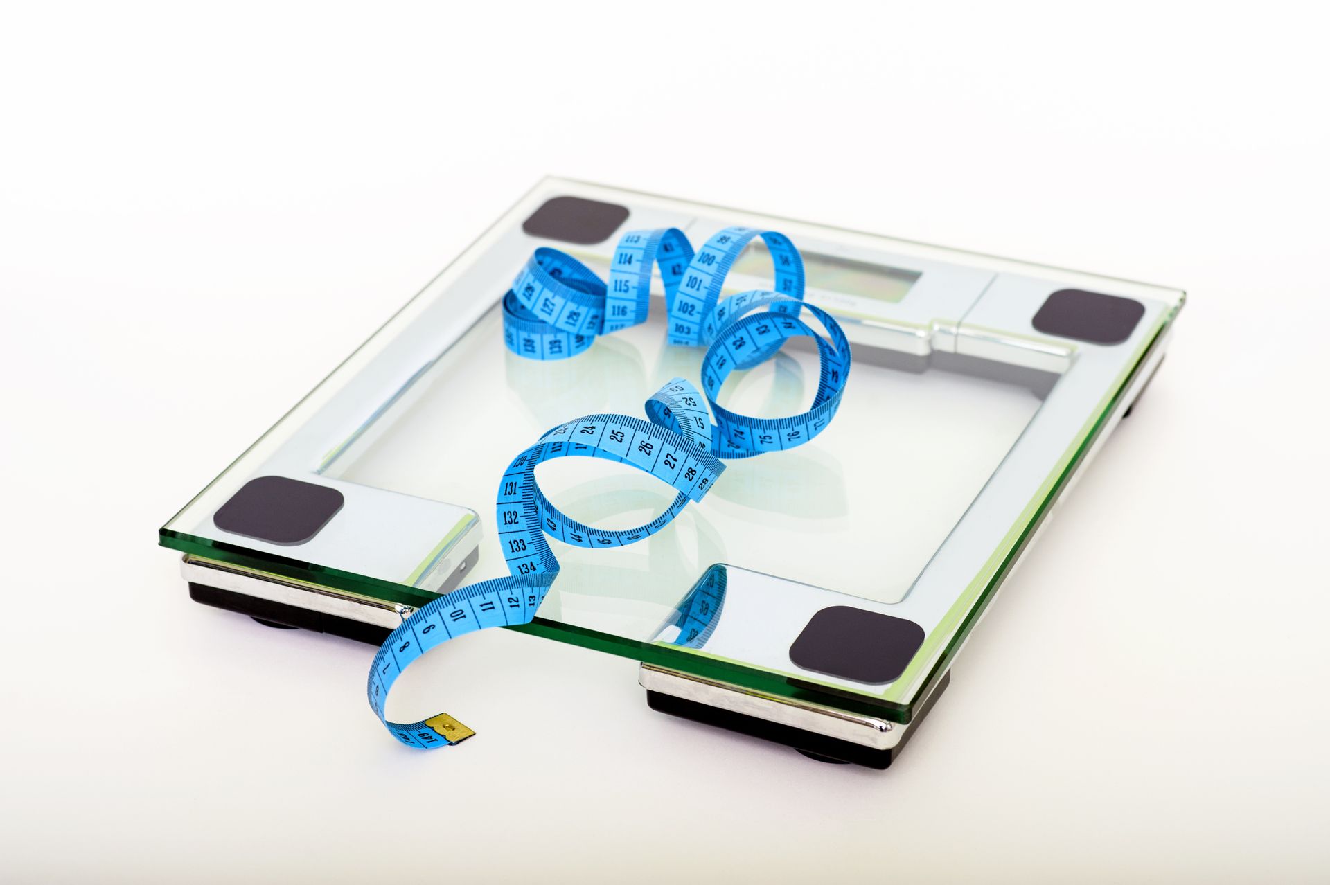 A glass bathroom scale with a blue measuring tape resting on top